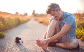Ein Mann sitzt draußen auf den Boden und massiert sich den Fuß